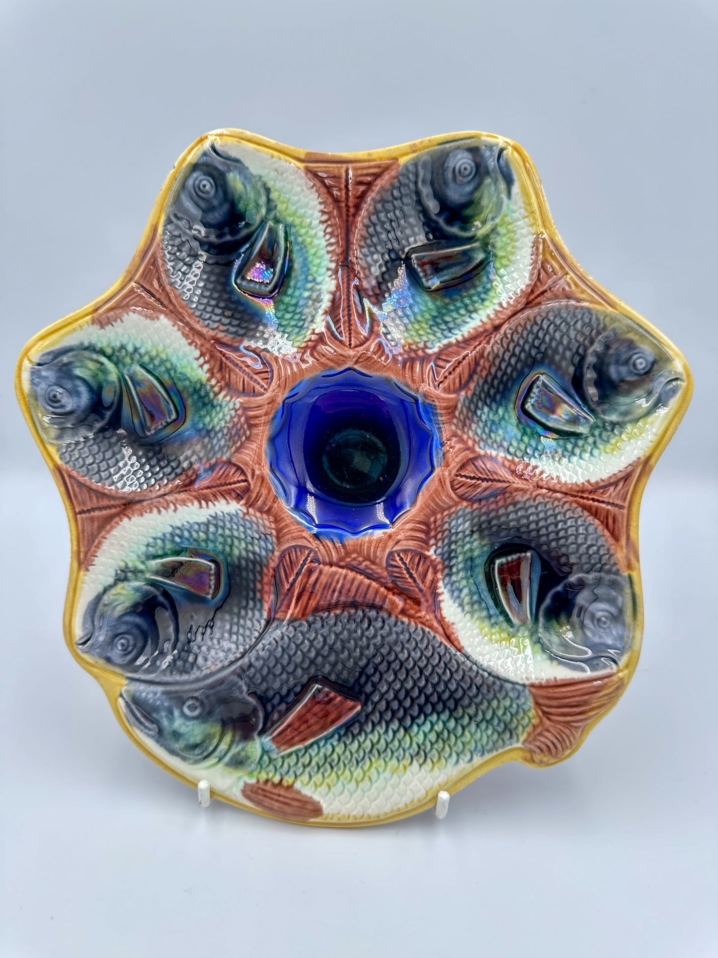 An Antique ceramic serving platter with a central blue cobalt well and surrounding yellow ochre rim, molded with six fish figures.