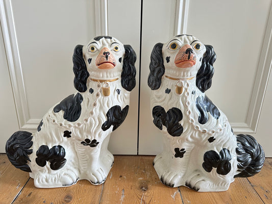A pair of large black and white Staffordshire Spaniel dogs with hand-painted facial expressions, sitting upright.