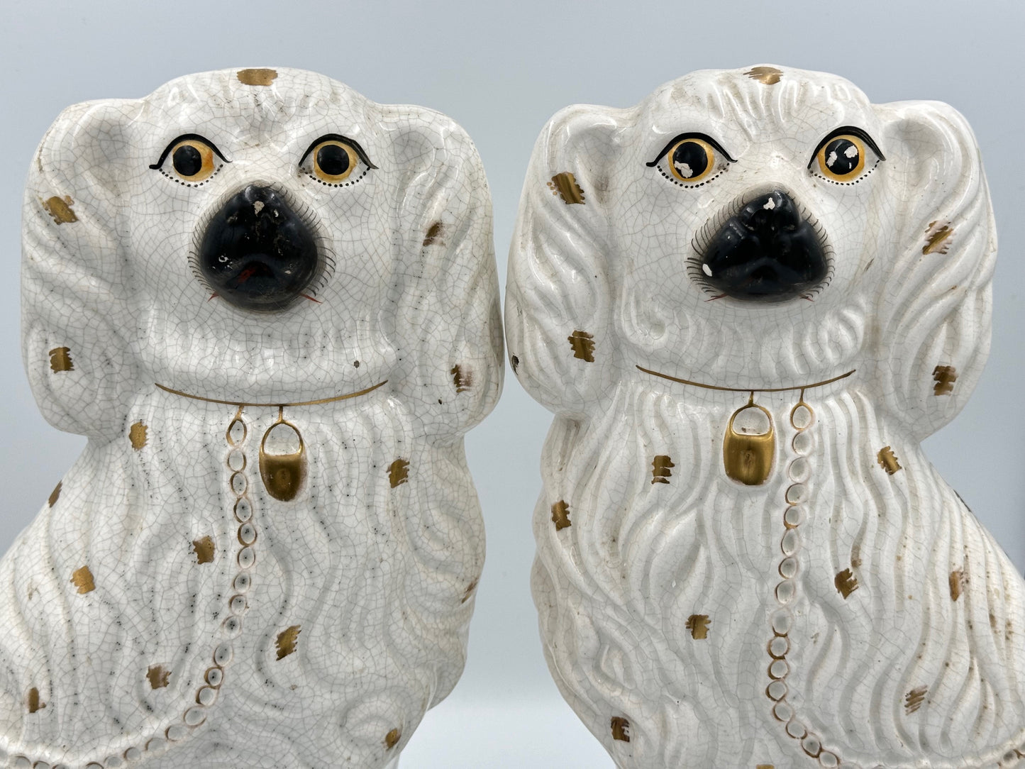 A pair of large ceramic Staffordshire Spaniel dogs in white with gold spots and decorative detailing.