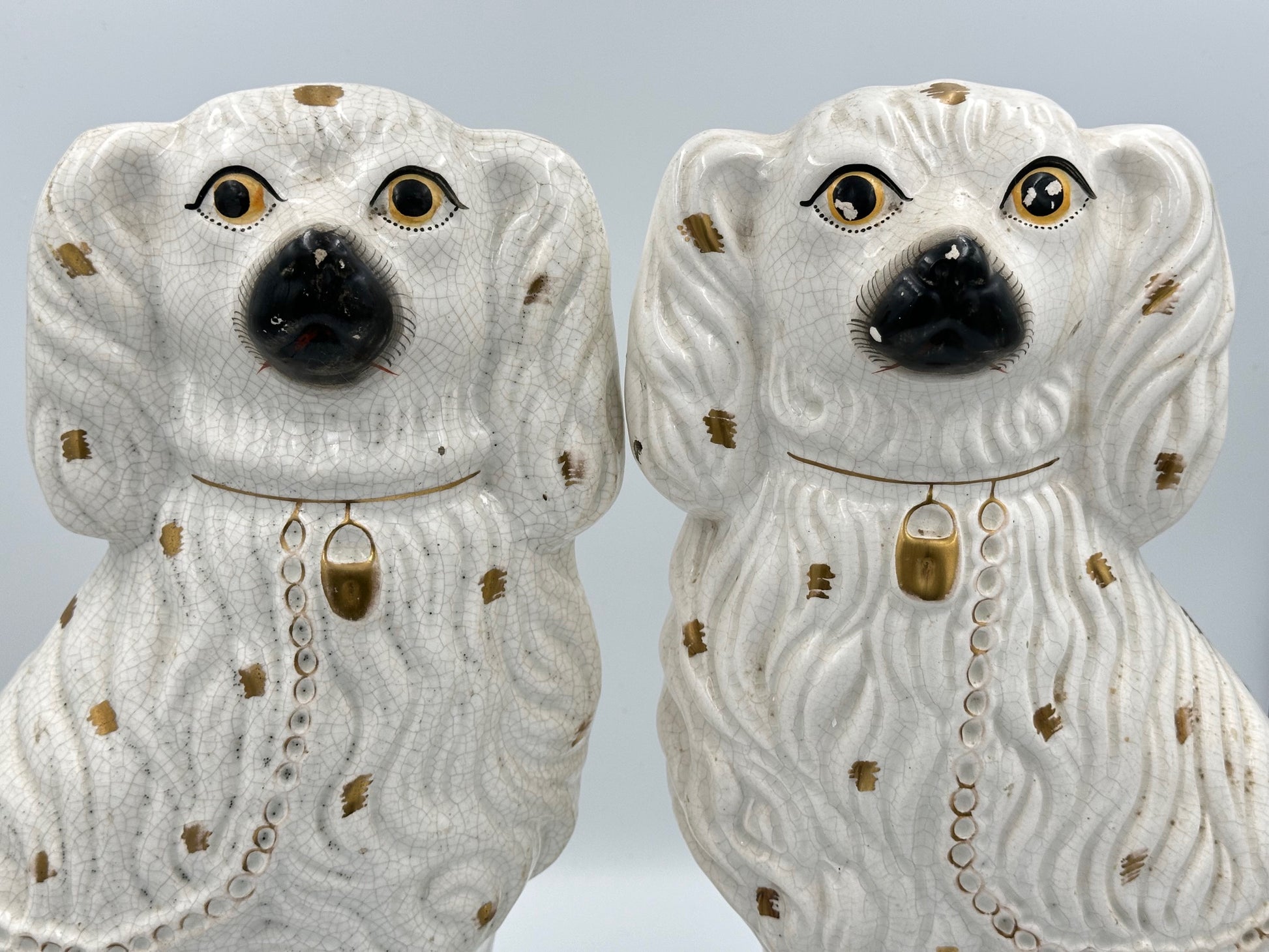 A pair of large ceramic Staffordshire Spaniel dogs in white with gold spots and decorative detailing.