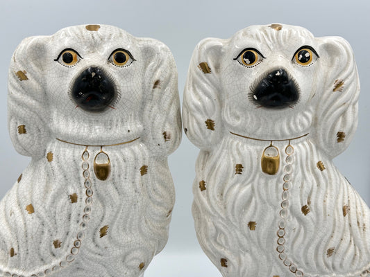 A pair of large ceramic Staffordshire Spaniel dogs in white with gold spots and decorative detailing.