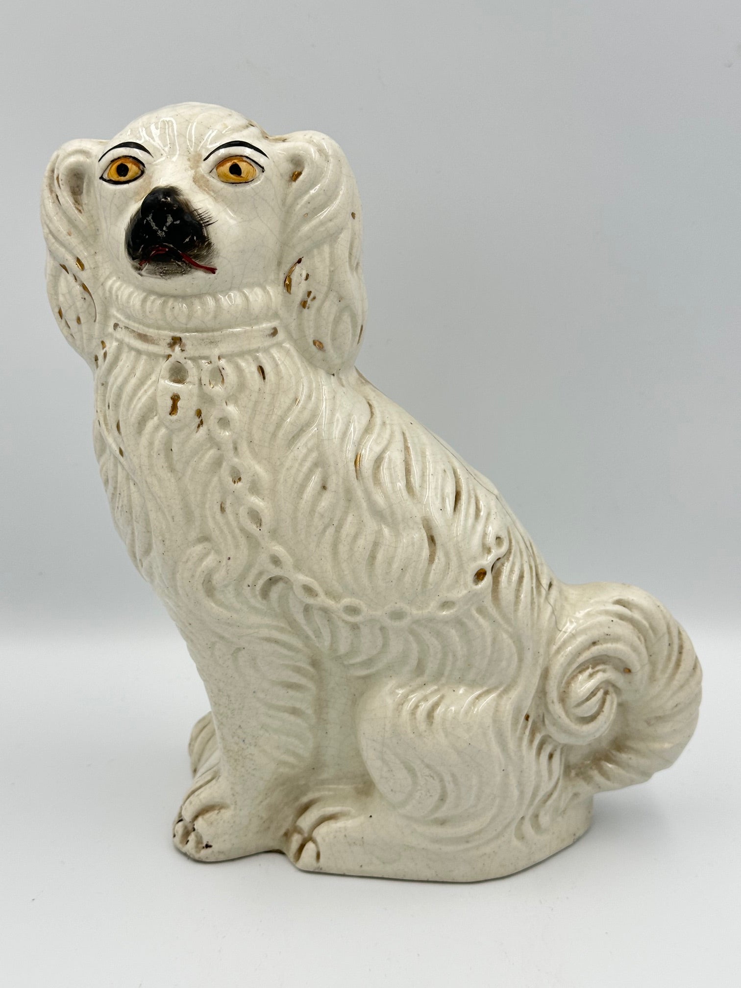Antique Staffordshire ceramic dog figurine with handpainted gilded accents, predominantly white with a detailed collar, lock, and chain.