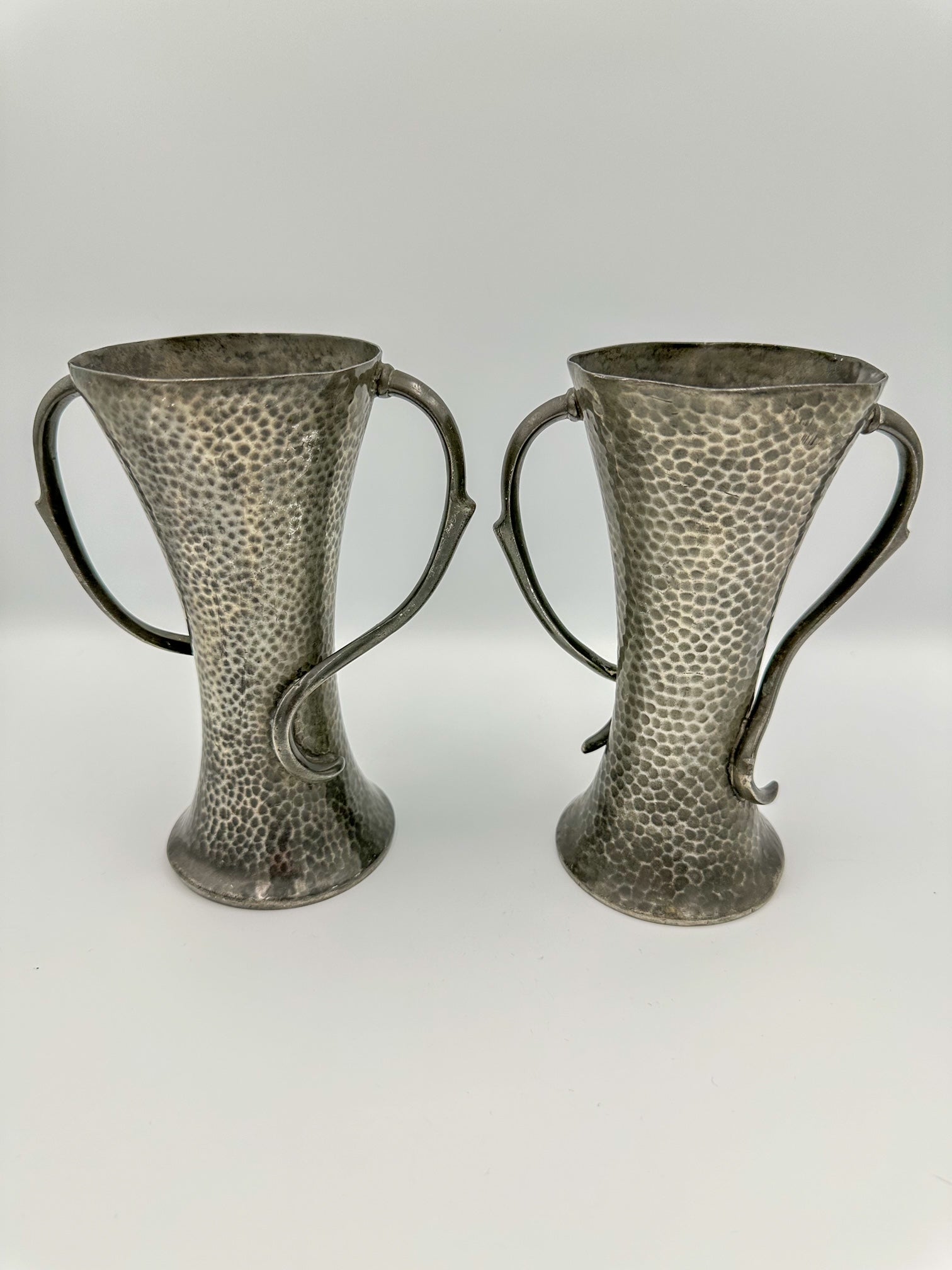 Two art nouveau pewter vases with a textured design, sitting side by side against a white background.