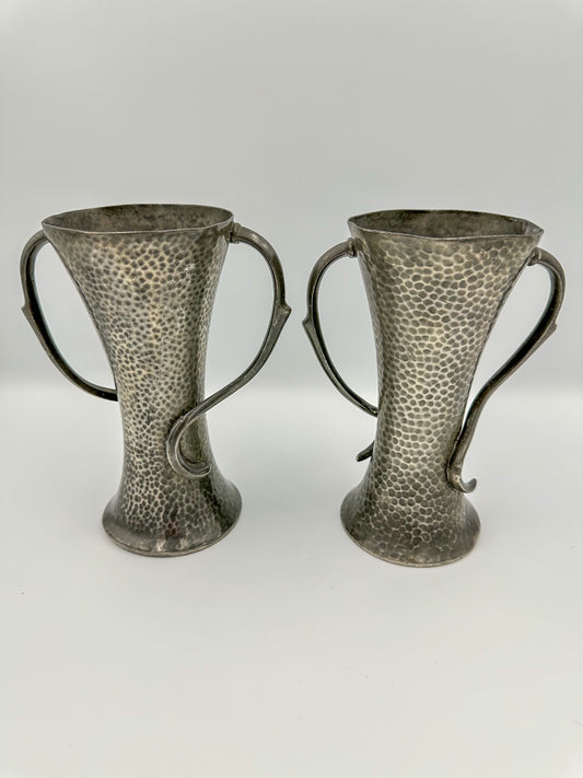 Two art nouveau pewter vases with a textured design, sitting side by side against a white background.