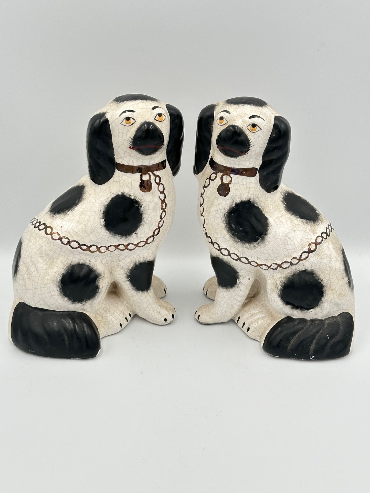 A pair of black and white Staffordshire King Charles Spaniel sculptures with hand painted faces, black spots, a gilt collar, lock, and chain.