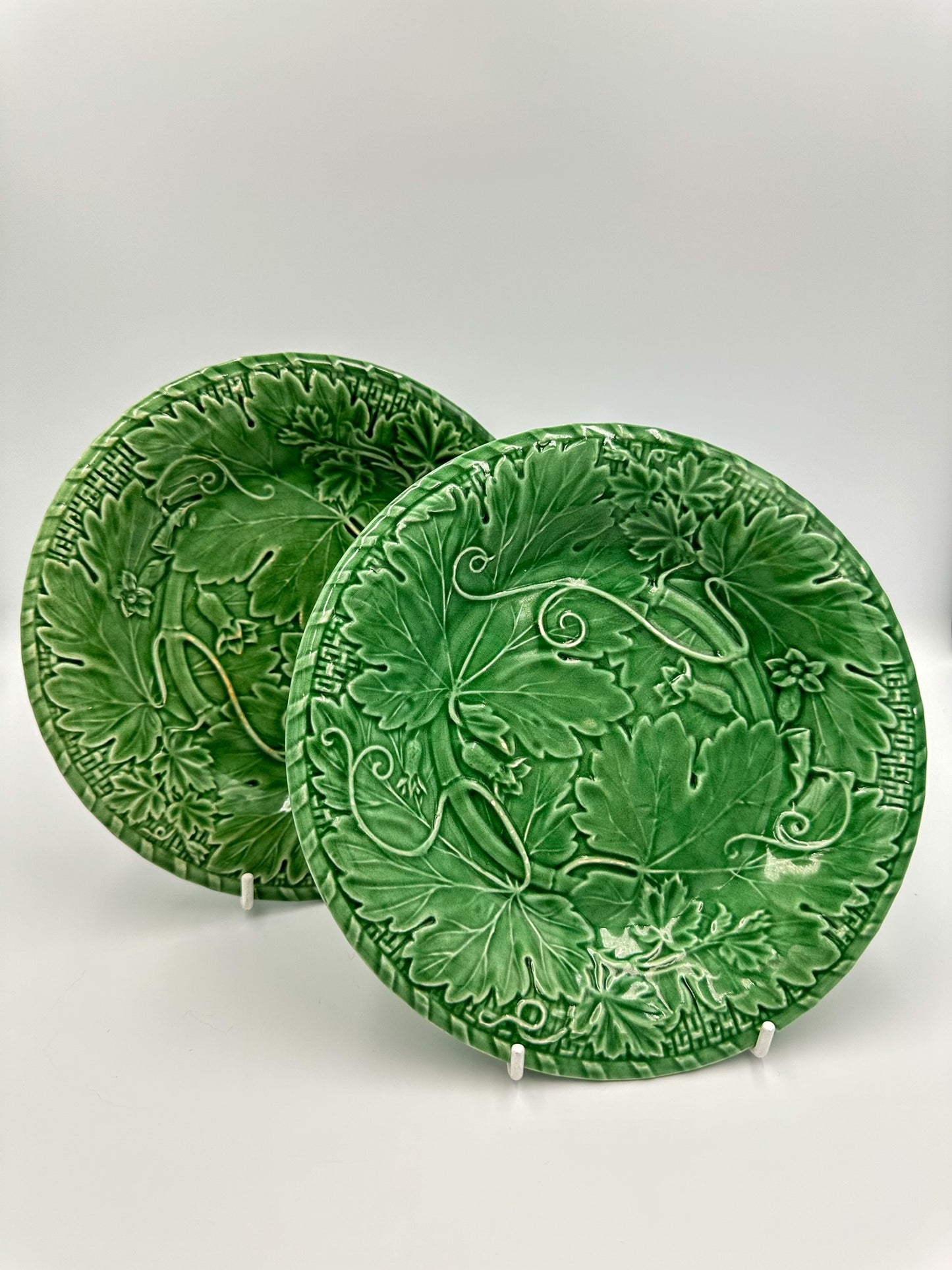 Two vintage green majolica plates with floral and vine patterns, displayed against a white background.