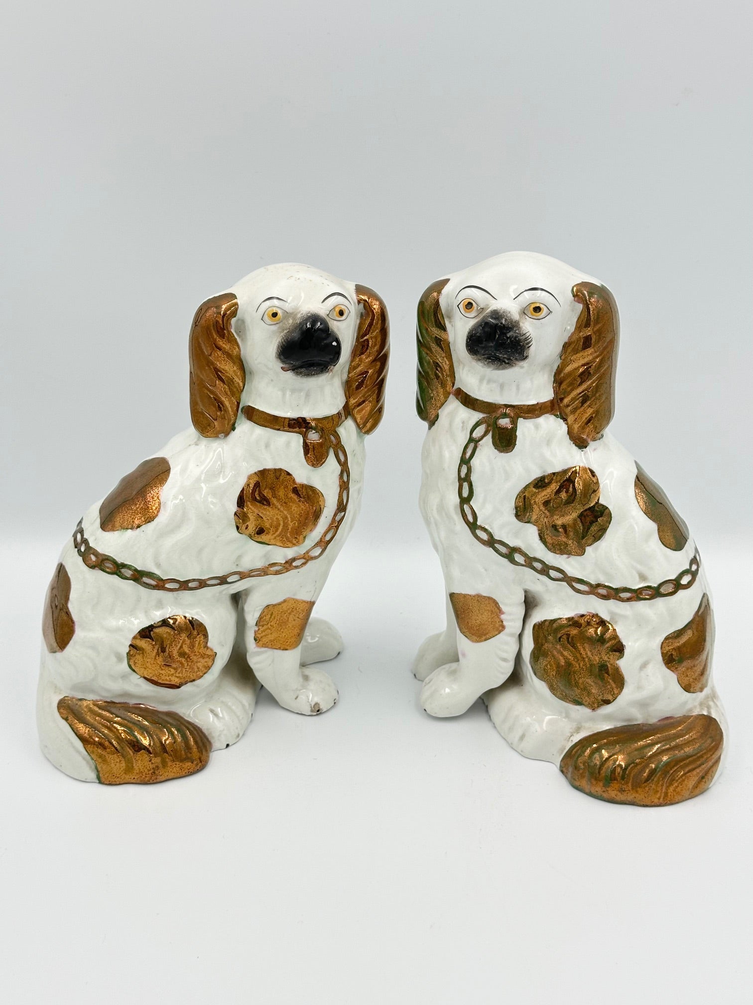 A pair of copper lustre Staffordshire King Charles Spaniels with separate legs, hand painted faces, and a chain detail.