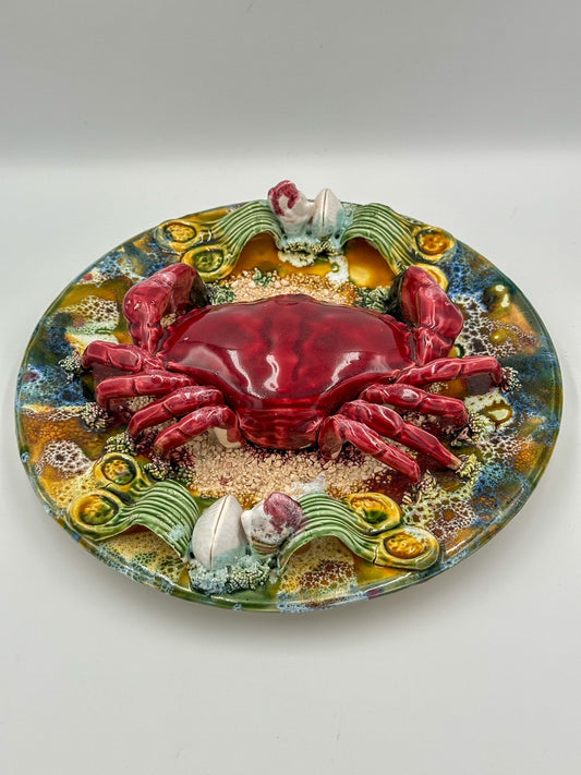A decorative majolica display plate featuring a realistic depiction of a red crab with a detailed shell, surrounded by sand and shells, on a colorful background with floral and marine motifs.