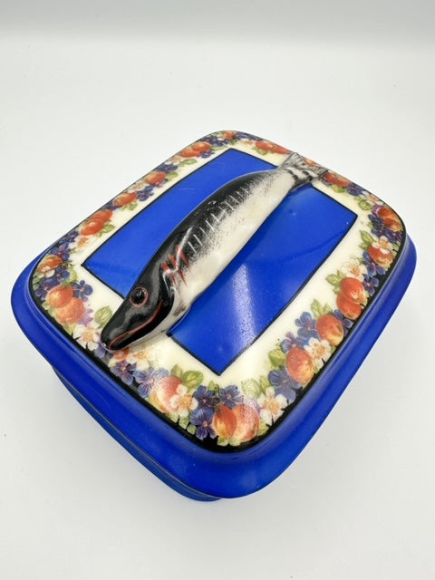 A blue porcelain sardine dish with a floral pattern around the edge and a fish handle on the lid.