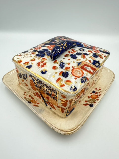 An ornate porcelain sardine dish with an Imari floral pattern, featuring gold and multicolored floral designs on a beige background, with a lid decorated in a similar style.
