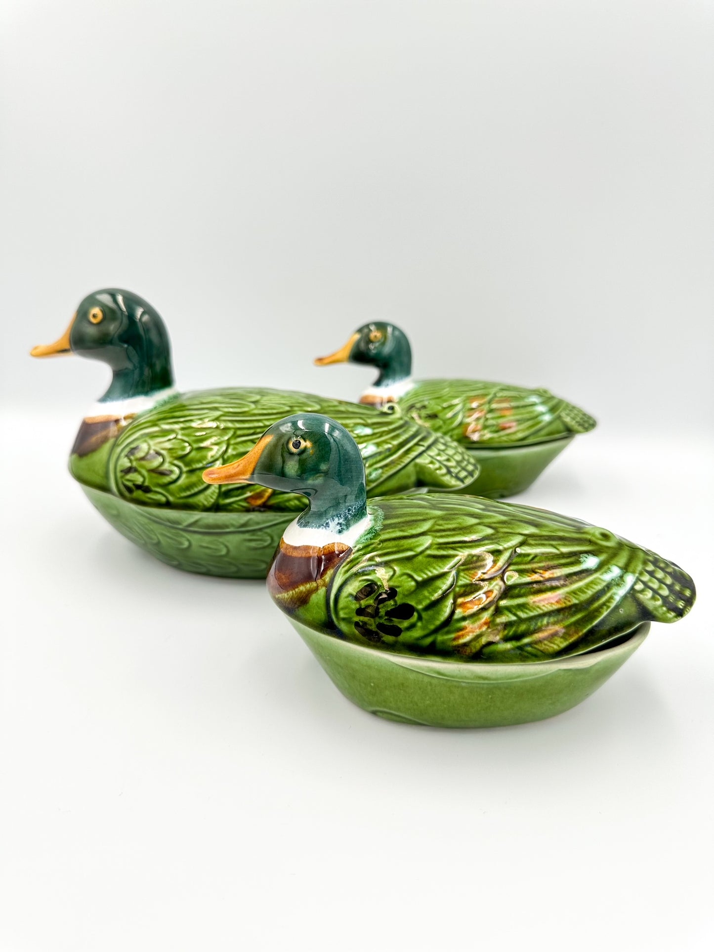 A set of three green and brown ceramic duck-shaped terrines with decorative lids.