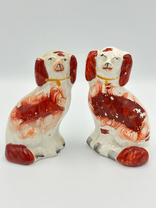 A pair of very small red Staffordshire King Charles Spaniels with handpainted markings and faces. They have gold collars and are seated.