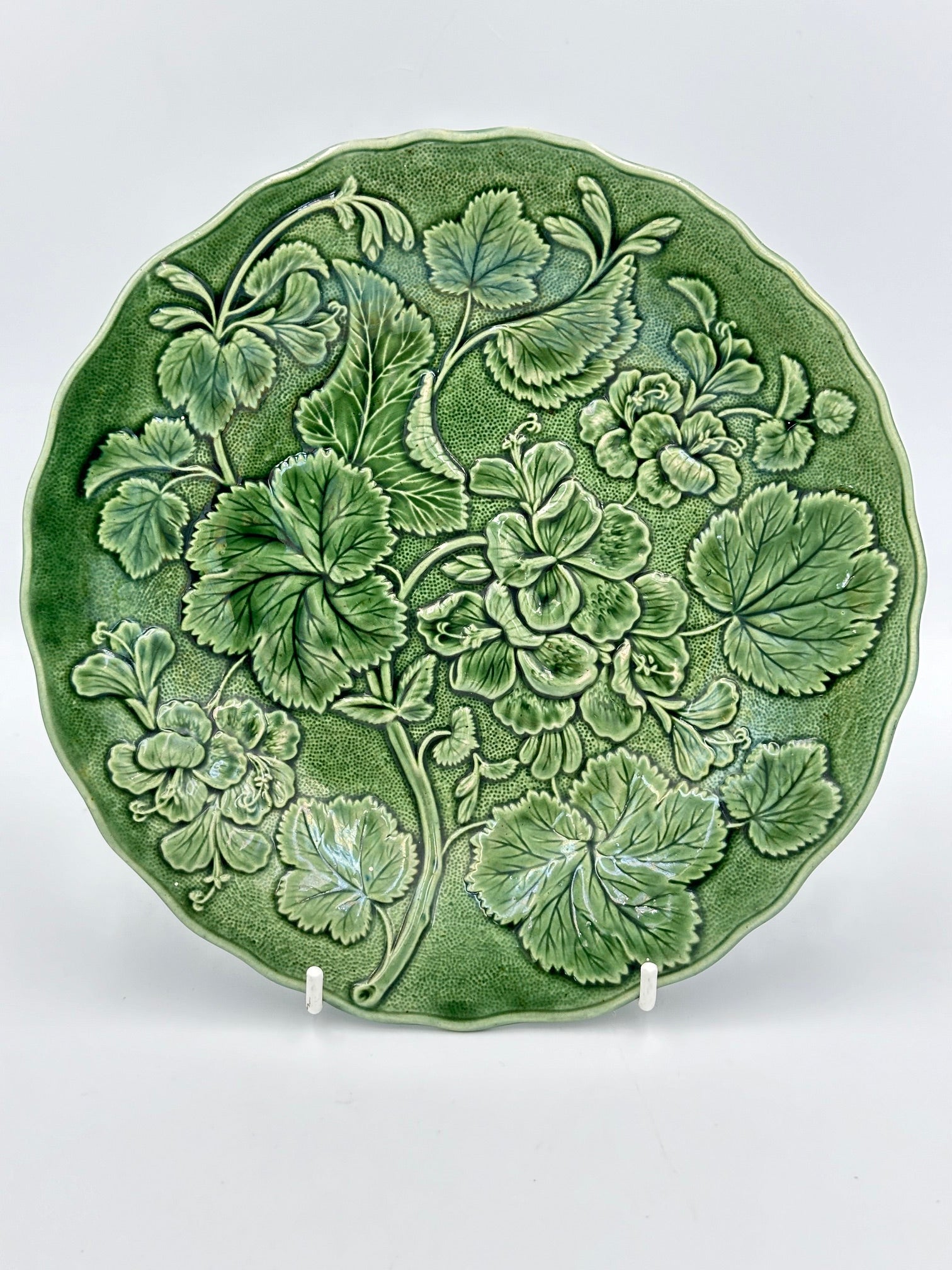 Vintage English Majolica ceramic plate with a floral and leaf pattern in sage green color, displayed on a stand.