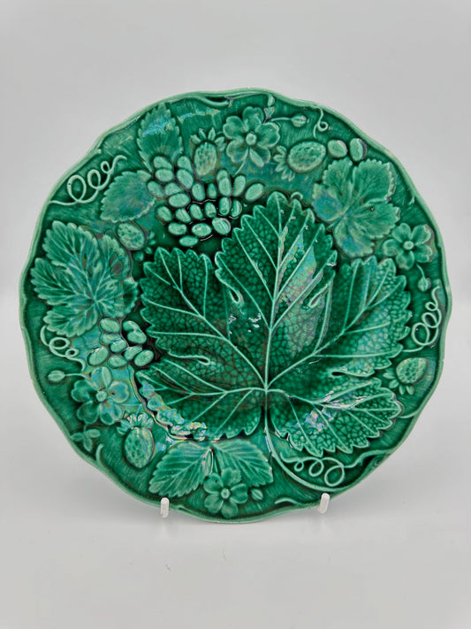 A round green majolica plate with a floral pattern, specifically grape leaves, featuring a deep green glaze.