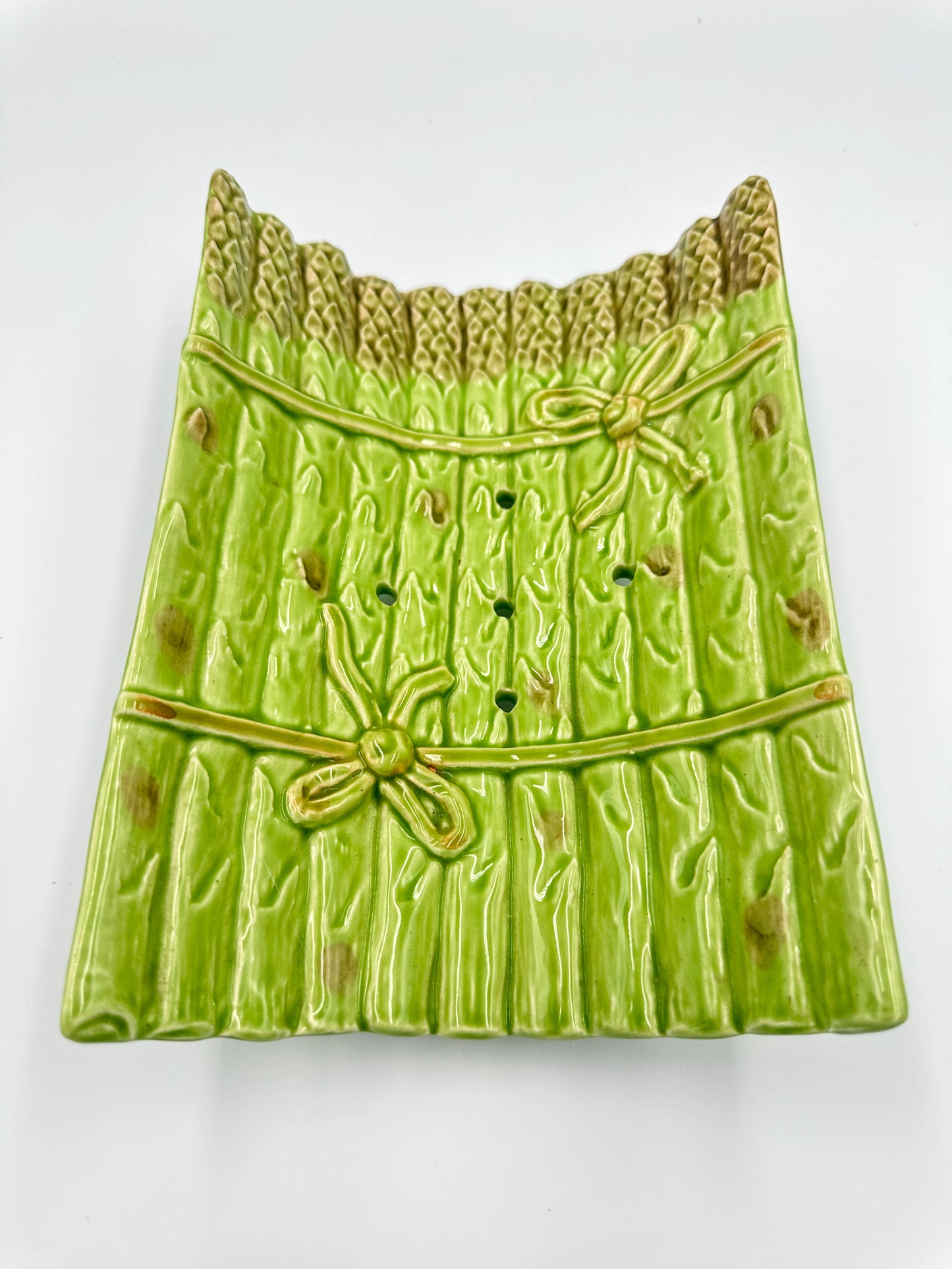 A vintage French Majolica ceramic asparagus-shaped serving dish with spring green and milk brown colors, featuring relief decoration of asparagus tied with ribbon, and a drainer plate on feet.