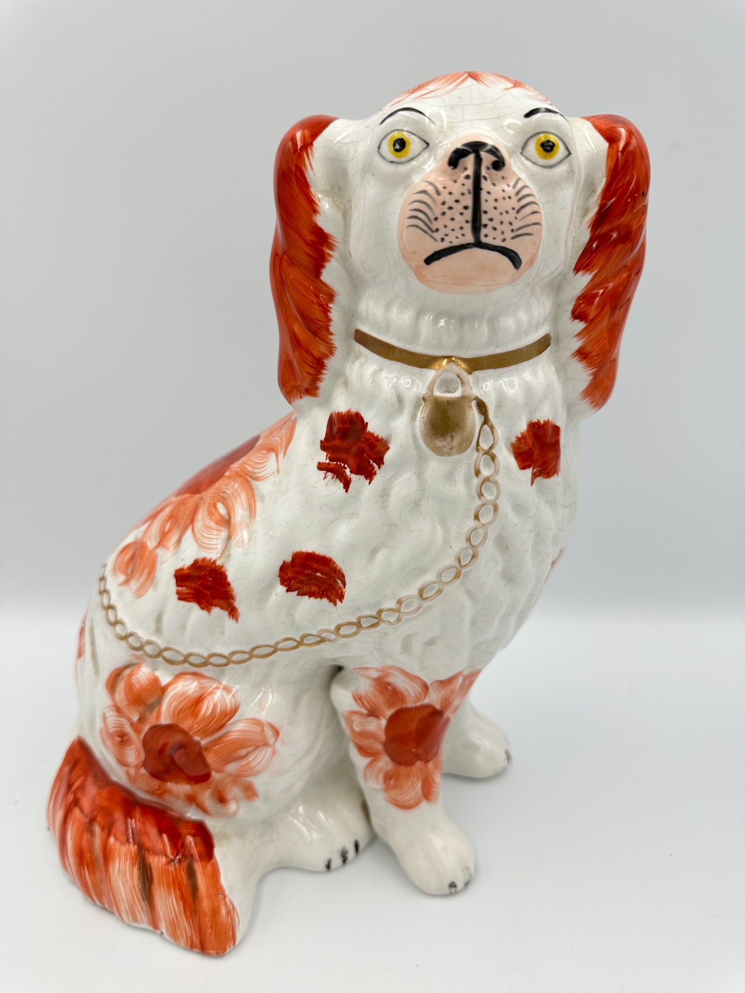 A red and white Staffordshire King Charles Spaniel with a gold collar and chain, featuring hand paintwork and floral-esque patterns.