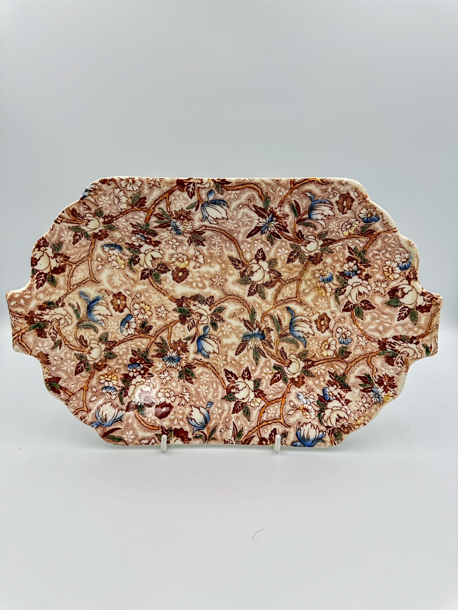 A brown and blue chintz ceramic serving dish with floral patterns on a white background.