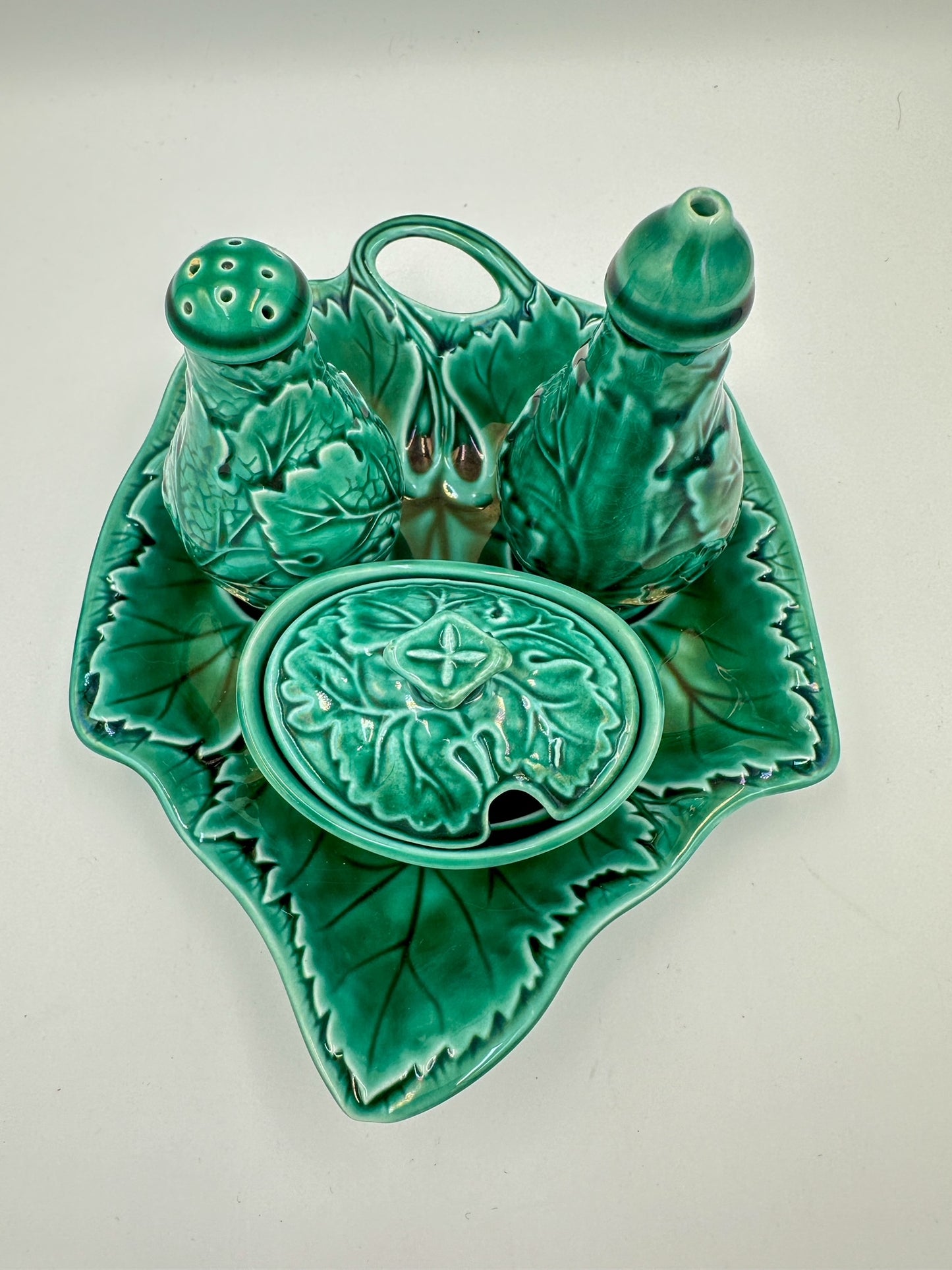 A green condiment set in majolica style. There is a salt shaker, jam server, and vinegar shaker. 