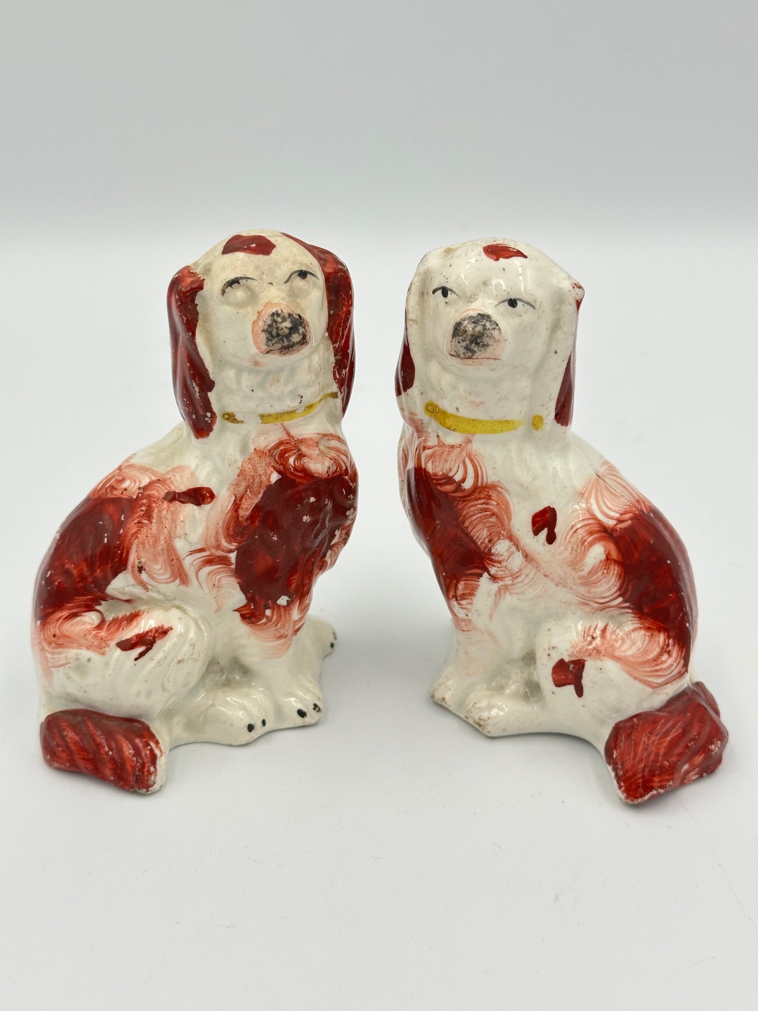 A pair of miniature red Staffordshire Spaniels with white and red paintwork, showing signs of wear and aging.