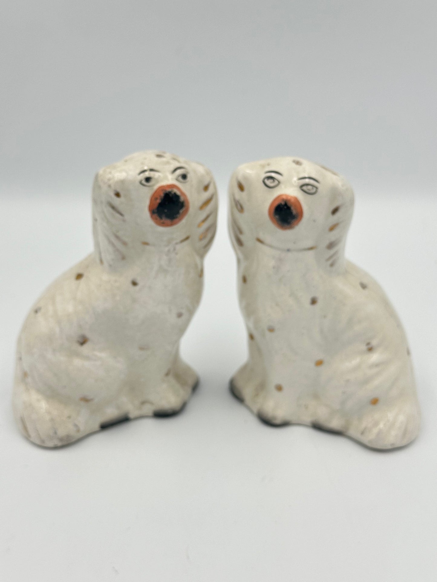 A pair of white ceramic Staffordshire Spaniels with gold paint marks, collars, and locks, exhibiting antique condition with some hairline cracks.