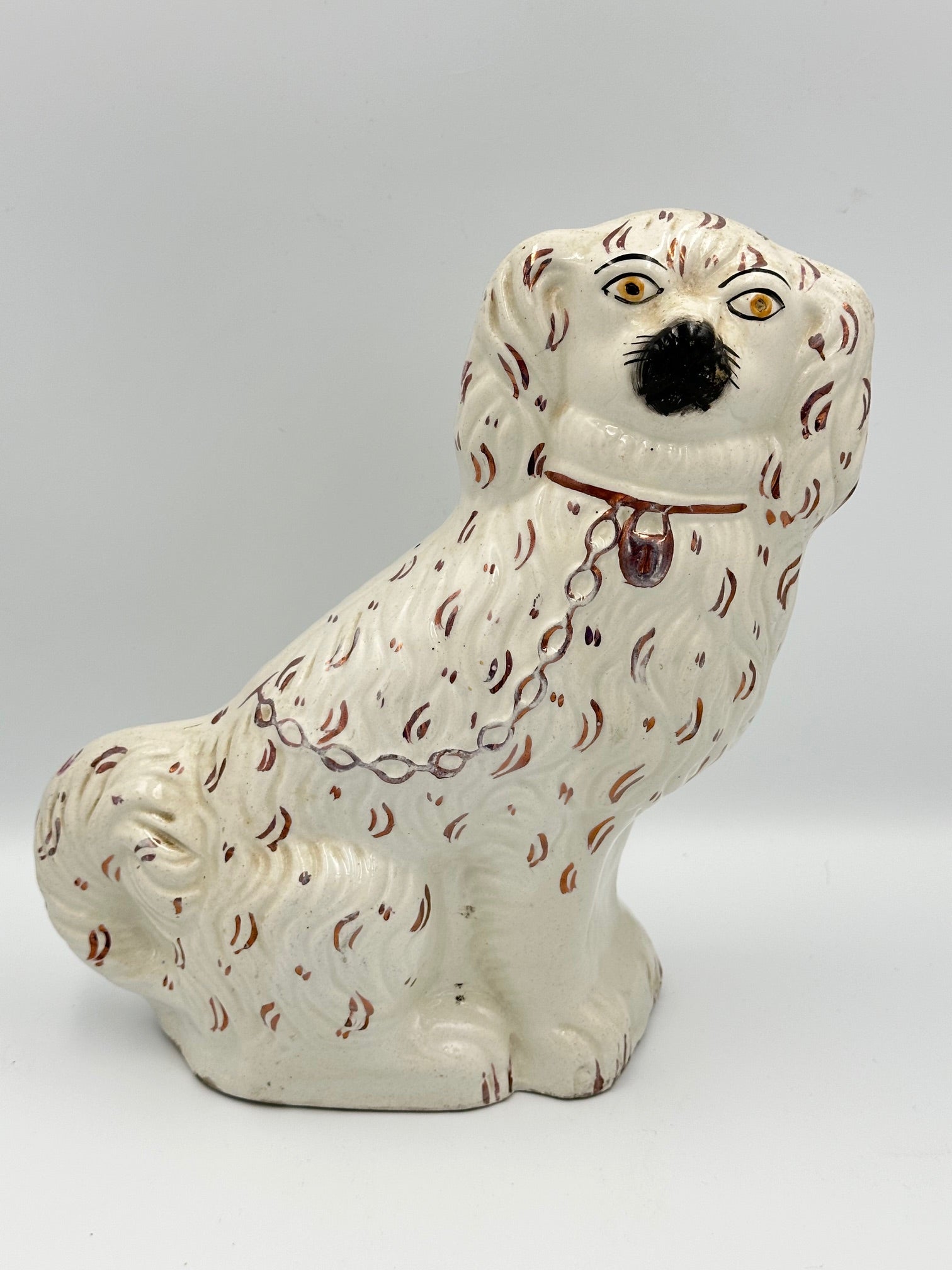 A single white Staffordshire Spaniel figurine with pink luster apostrophe like details painted on it. 