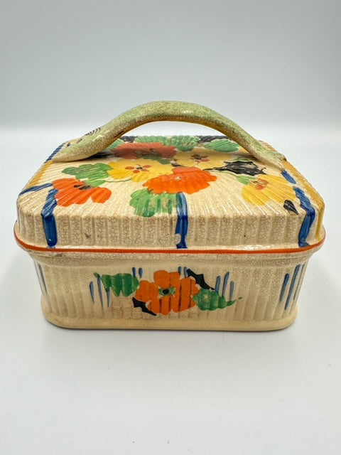 A rectangular Podmore Hanley Art Deco sardine dish with a floral pattern, predominantly cream color, with poppies in orange and green, and a green fish handle on the lid.