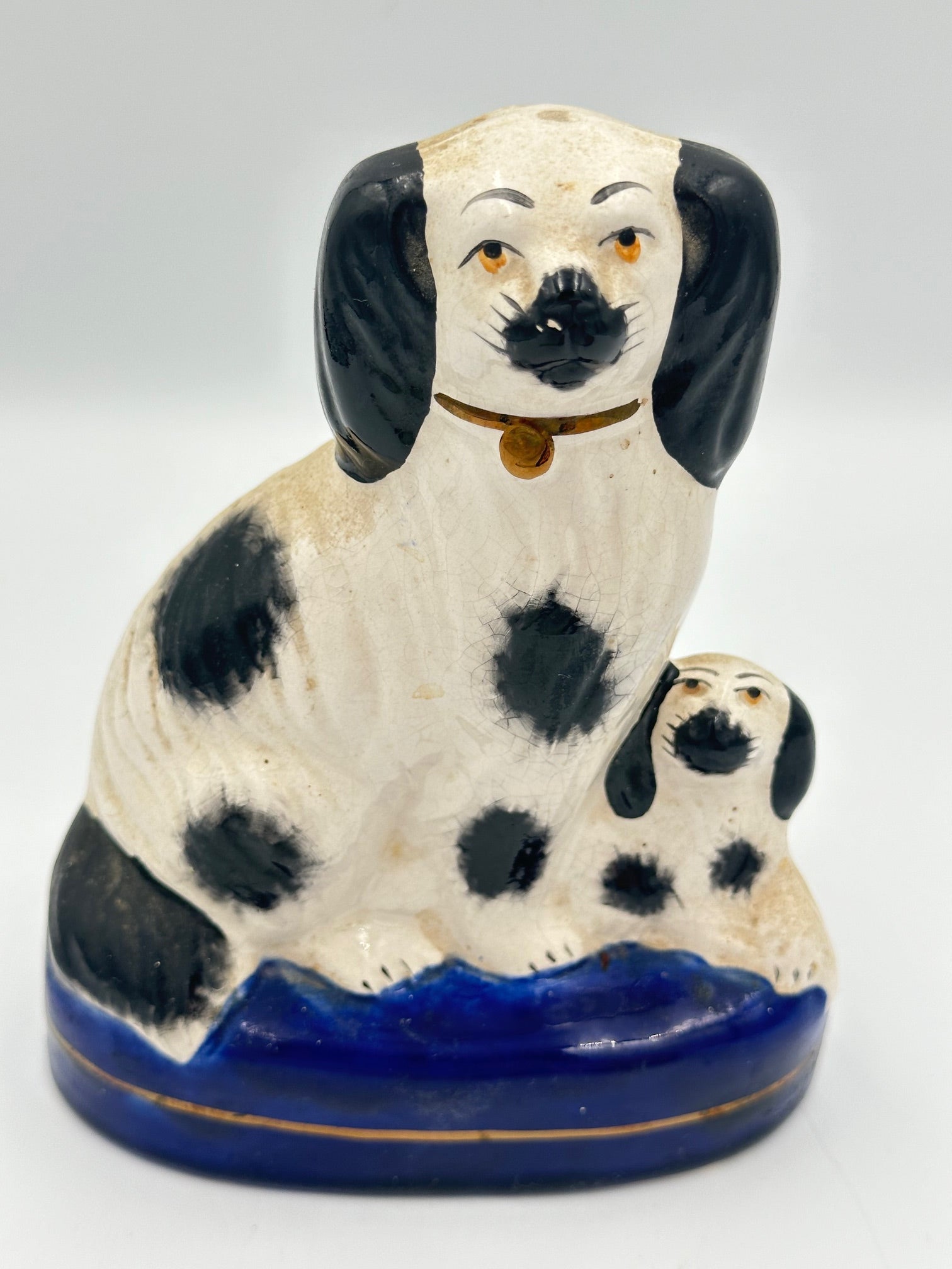 A black and white Staffordshire Spaniel dog and its puppy on a cobalt blue base with a gold stripe, hand painted.