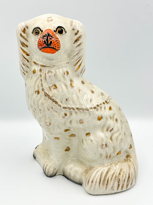 A vintage white ceramic figurine of a King Charles Spaniel with hand painted gold markings, a gold collar, lock, and chain. The figure has a sweet facial expression and is posed with a slight tilt to the side.
