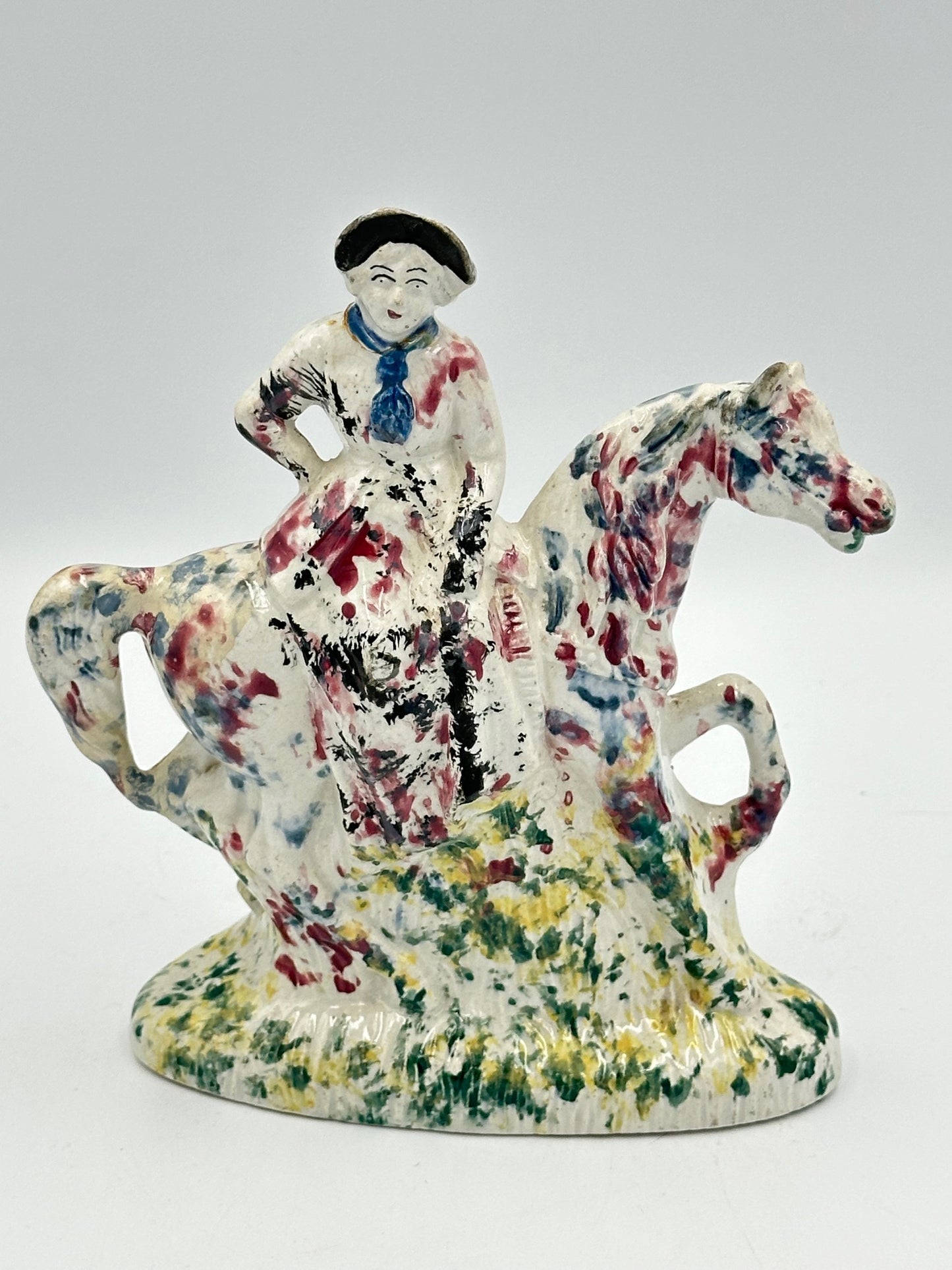 Antique ceramic figurine of a woman on a horse with sponge painted decoration in multiple colors.
