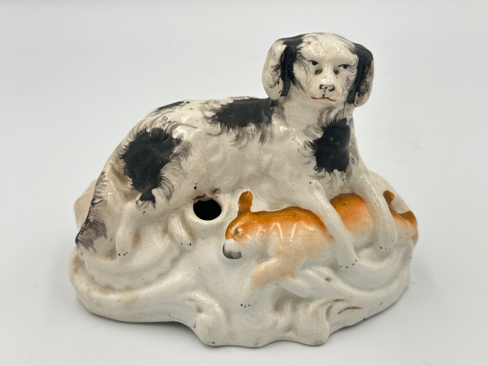 A Staffordshire pottery figurine depicting a black and white spotted hunting dog with a prize hare, handpainted in the mid-1800s.