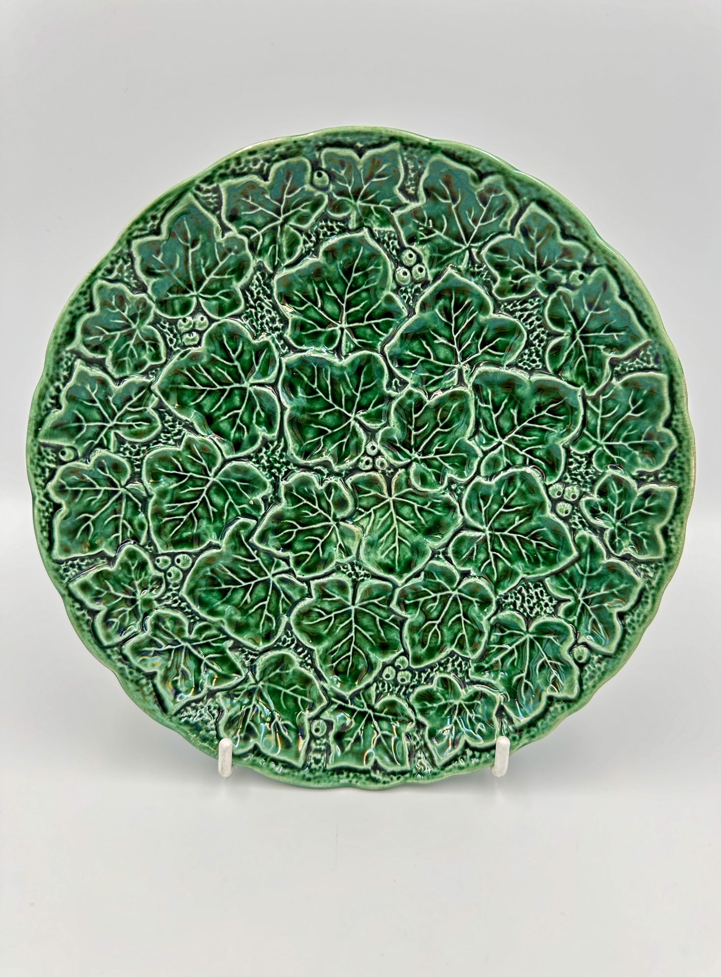 A round green majolica plate with a detailed ivy leaf pattern, made in England in the early 20th century.