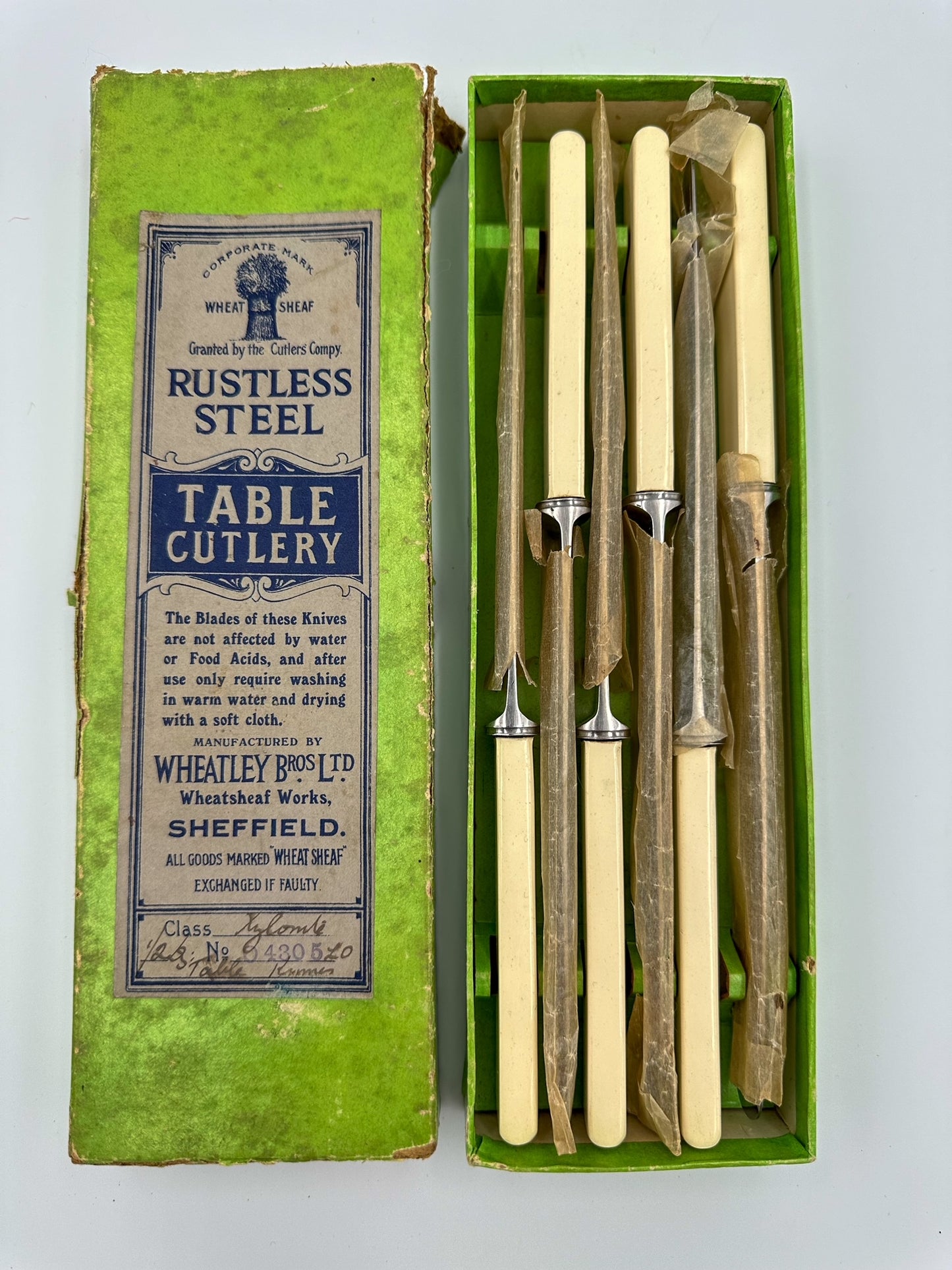 A set of six vintage stainless steel and Bakelite dinner knives still wrapped in waxed paper, displayed in an open box with a label reading 'RUSTLESS STEEL TABLE CUTLERY'.