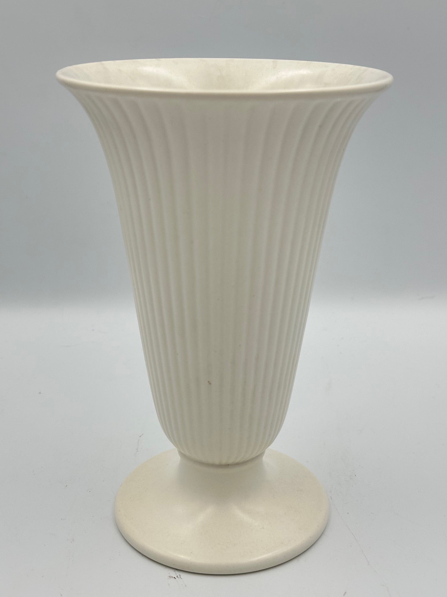 A white, ribbed, fluted trumpet vase with a footed base.